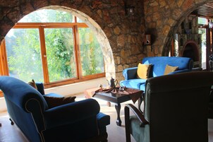 Una habitación acogedora con paredes de piedra, un amplio ventanal de arco y una chimenea.