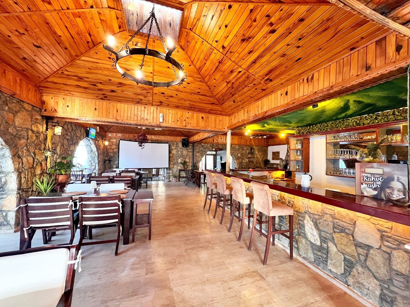 A rustic wooden interior with a bar area, stone walls, and a large screen.