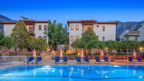 A swimming pool with lounge chairs and umbrellas, surrounded by buildings with balconies and trees.