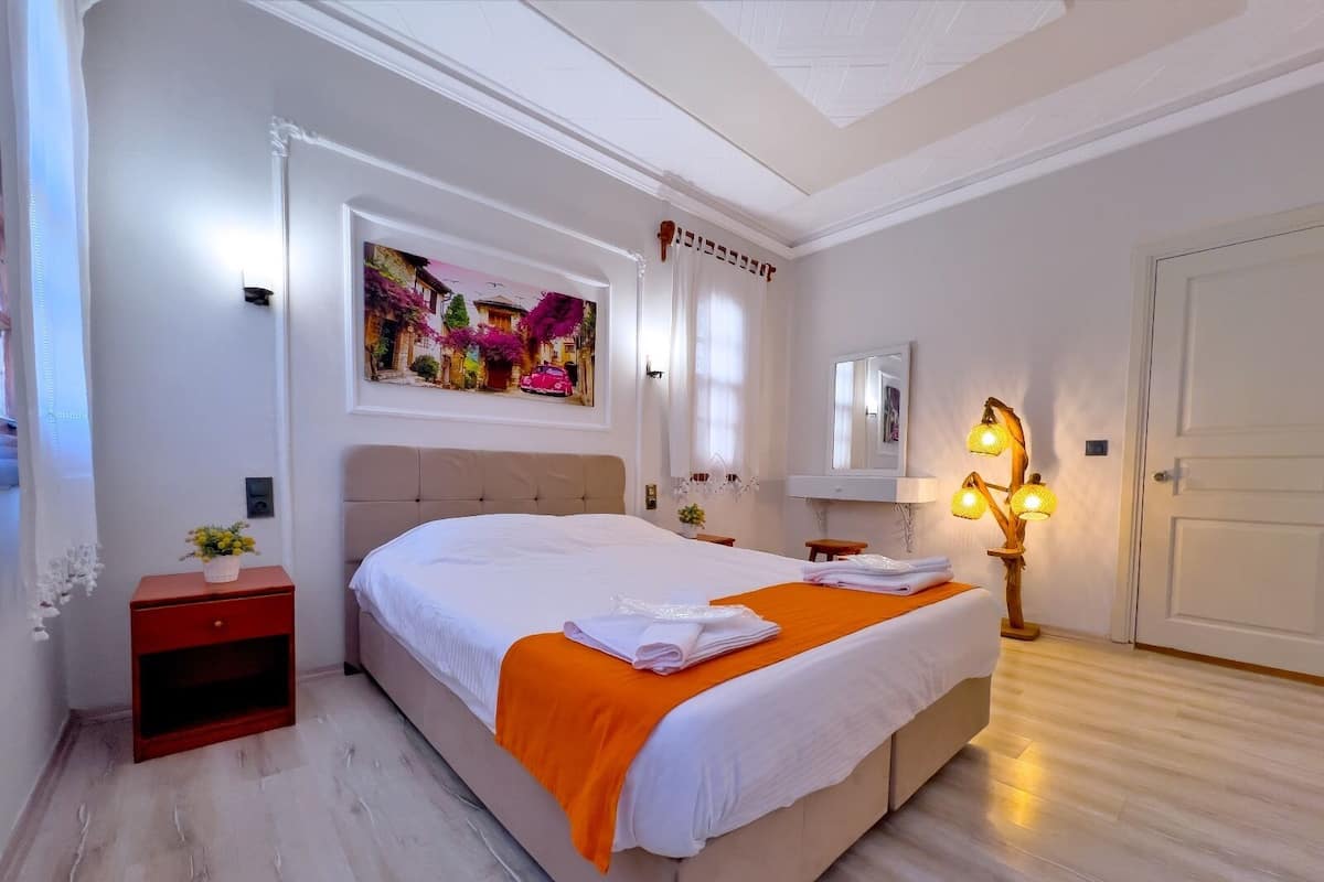 A bedroom with a large bed, a nightstand, a wall-mounted mirror, and a painting above the bed.