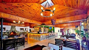 A spacious lodge with a high wooden ceiling, a stone fireplace, a bar area, and multiple seating arrangements.
