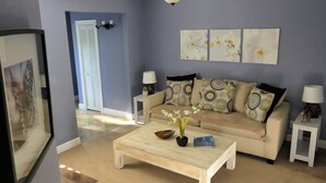 A living room with a beige sofa, patterned cushions, a coffee table with a bowl and plant, and a ceiling fan. - Sun, beach, and great savings: huge discounts on holiday destinations! (Fort Myers)