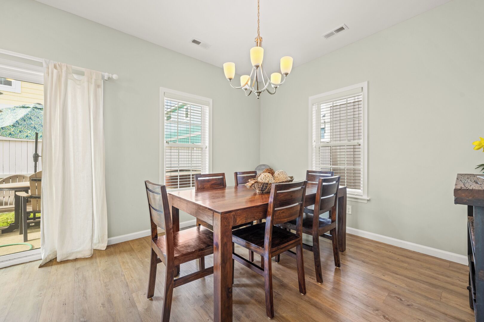 A dining room with a wooden table and chairs, a chandelier, and windows with blinds.