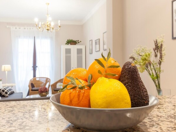 A bowl of fruits on a kitchen counter with a dining area in the background.
