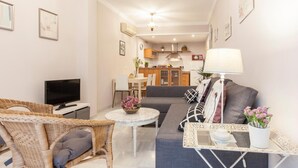 A modern living room with a sofa, chairs, a TV, and a dining area in the background. - Elegant 2 BR in the heart of Seville.A / C / WIFI AV (SEVILLA)