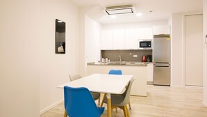 Una cocina moderna con armarios blancos, un microondas y un refrigerador. Hay un comedor con una mesa blanca y sillas azules.
