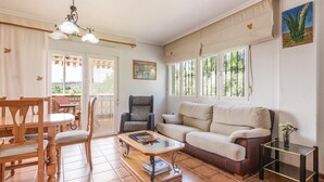Una sala de estar con sofá, una mesa de centro, una silla y una mesa de comedor. Hay una ventana que ofrece vistas a zonas verdes.
