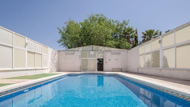 Una piscina rectangular con borde de azulejos, rodeada por un muro blanco con ventanales grandes.