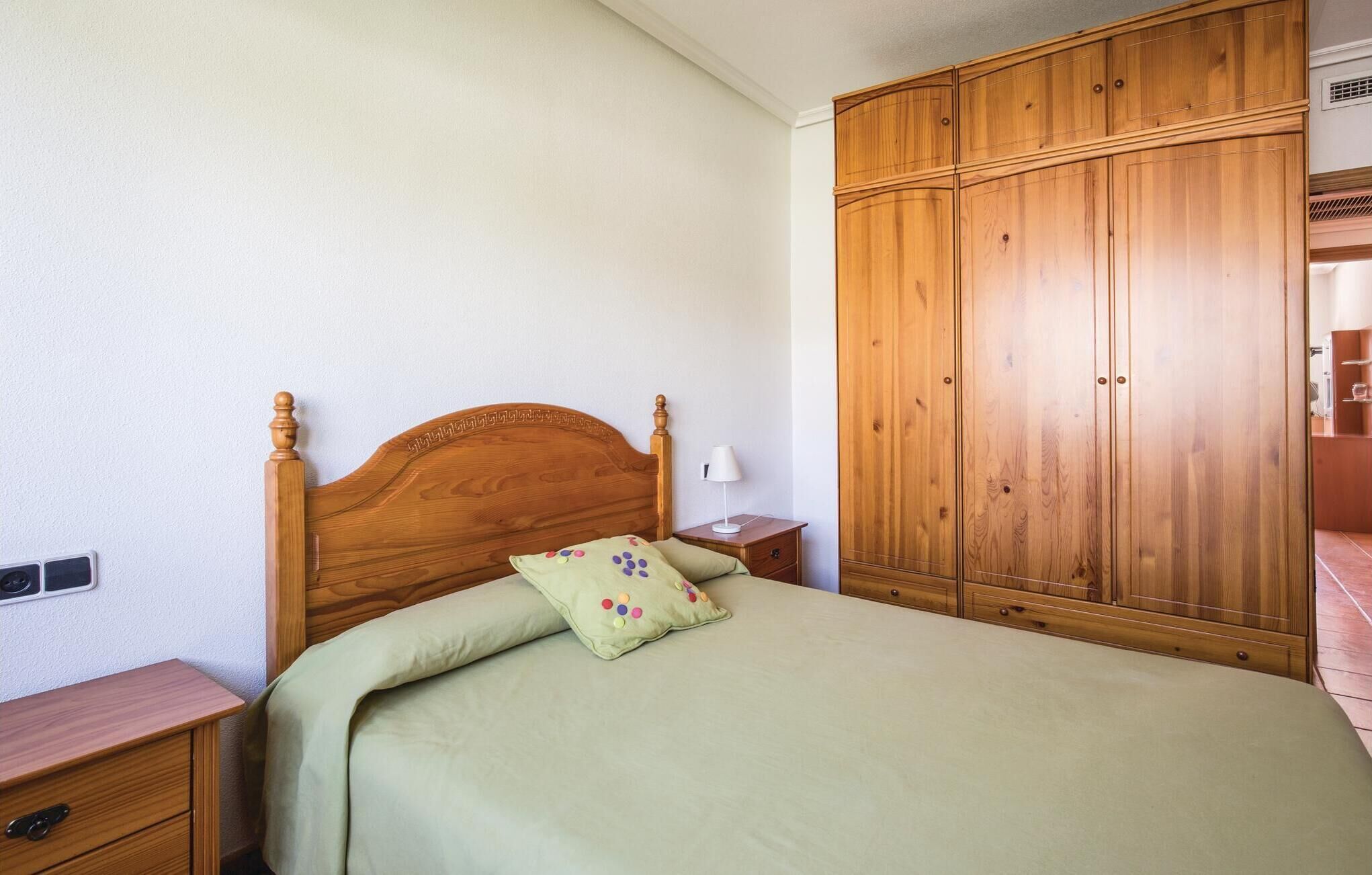 A bedroom with a wooden bed, a nightstand, a wardrobe, and a wall-mounted shelf.