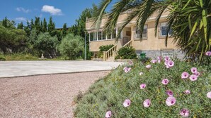 Un edificio con fachada de piedra, camino de hormigón y zona de grava con flores moradas.