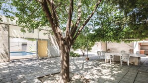 Un patio trasero con un árbol, una piscina y mobiliario exterior.
