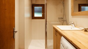 A modern bathroom with a wooden ceiling, a glass shower enclosure, a white sink, and a wooden vanity. - Spacious, Bright 3*** Apartment with WIFI (La Clusaz)
