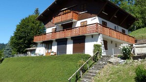 A chalet-style building with a wooden balcony, stone steps, and a clear view of the surrounding greenery. - Spacious, Bright 3*** Apartment with WIFI (La Clusaz)