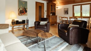 A cozy living room with a wooden ceiling, a fireplace, a dining area with a table and chairs, and a kitchen area with cabinets. - Spacious, Bright 3*** Apartment with WIFI (La Clusaz)