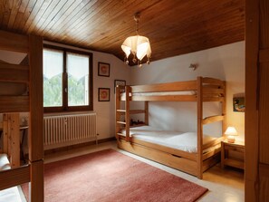 A wooden bunk bed room with a radiator, a window with a view of greenery, and a hanging light fixture.