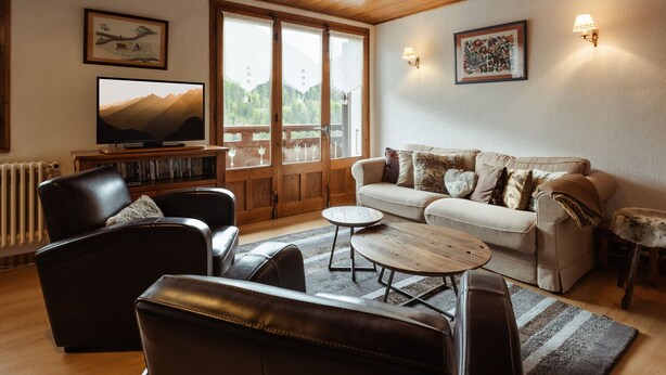 A cozy living room with a wooden ceiling, a television, a sofa, a coffee table, and a fireplace. - Spacious, Bright 3*** Apartment with WIFI (La Clusaz)