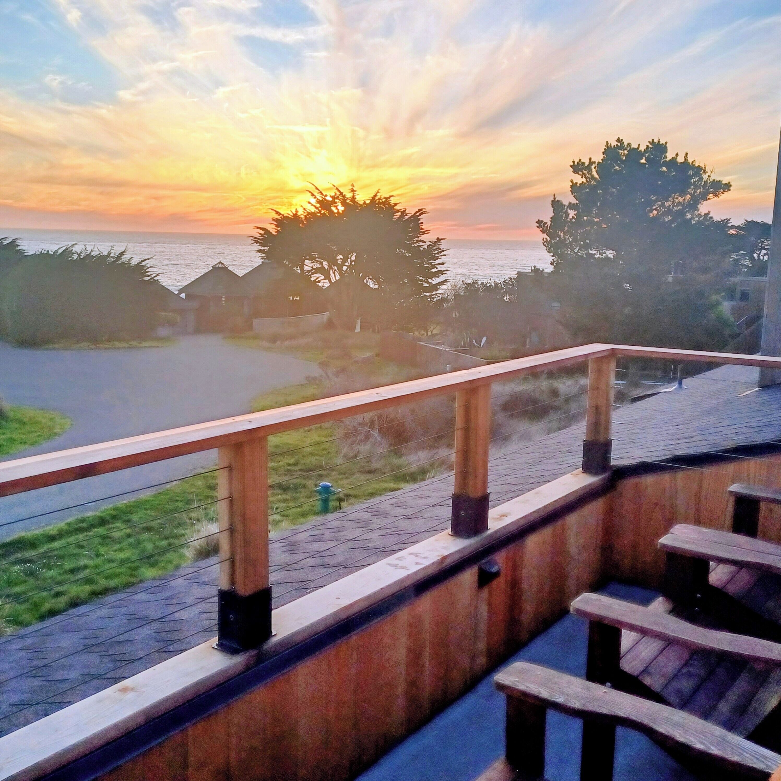 A wooden deck with a railing overlooking a beach and ocean during sunset.
