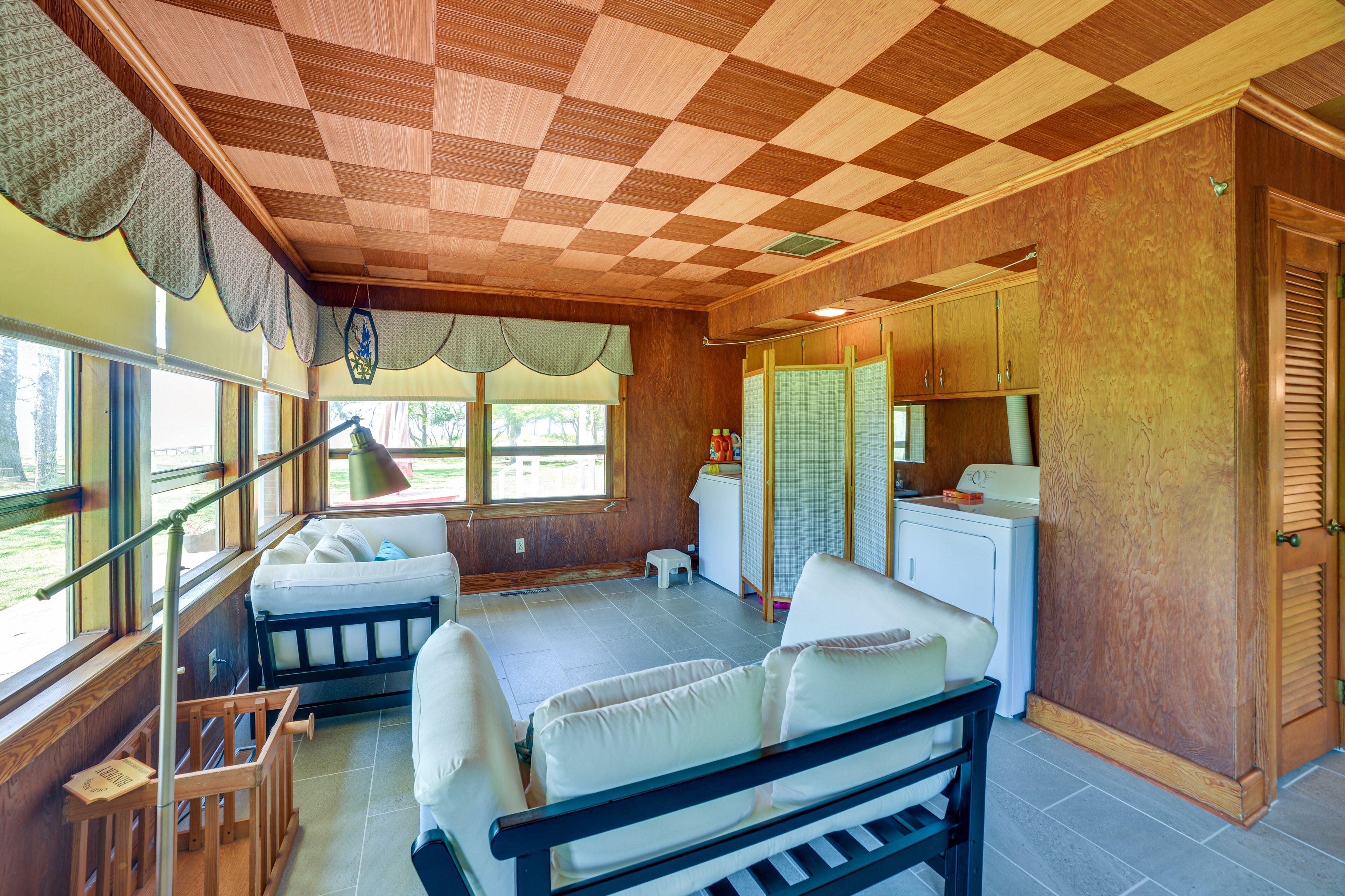 A room with a checkered ceiling, a bed, a small table, and a window with curtains.