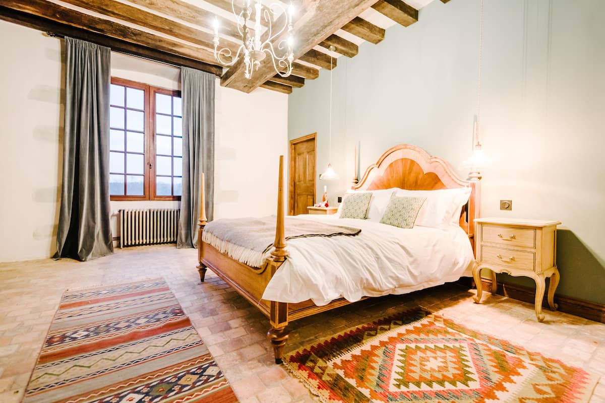 Quarto com uma cama de dossel de madeira, mesa de cabeceira, cômoda e uma janela grande com cortinas.