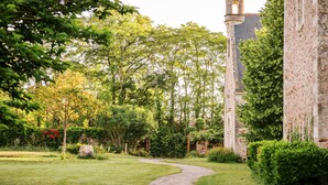 A stone building with a tower, surrounded by lush greenery and a winding path.