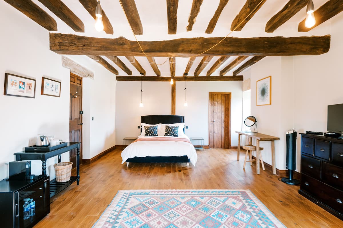 Quarto com teto de madeira, cama com almofadas estampadas, escrivaninha com cadeira e televisão.