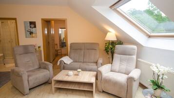 A modern living room with a skylight, two beige armchairs, a wooden coffee table, and a potted orchid.
