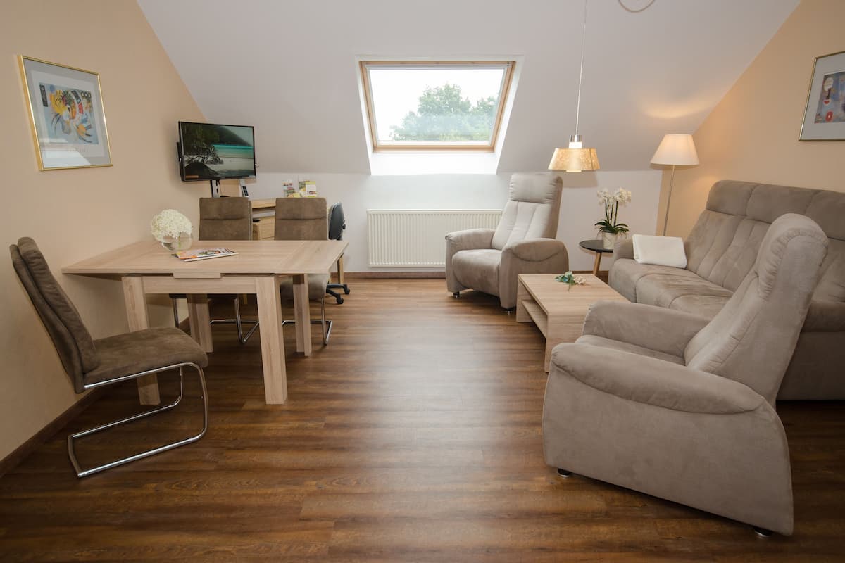 A modern living room with a dining area, a sofa, a chair, a TV, and a window with a view.
