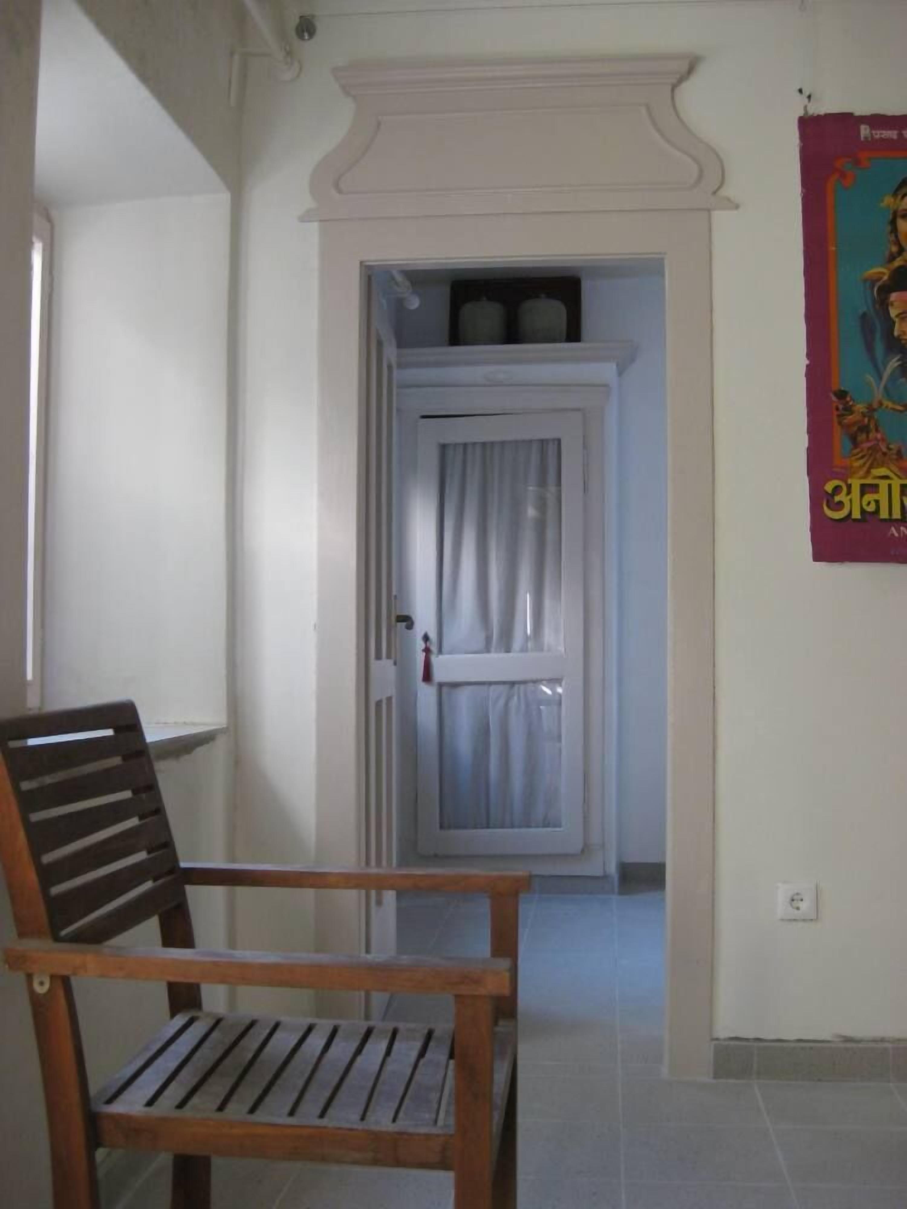 A hallway with a wooden chair, a white door with a curtain, and a poster on the wall.