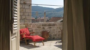 A balcony with a red chair, a stone wall, and a view of distant buildings and hills.