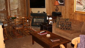 Un salon chaleureux avec une cheminée, des meubles en bois, un téléviseur et un tableau accroché au mur.