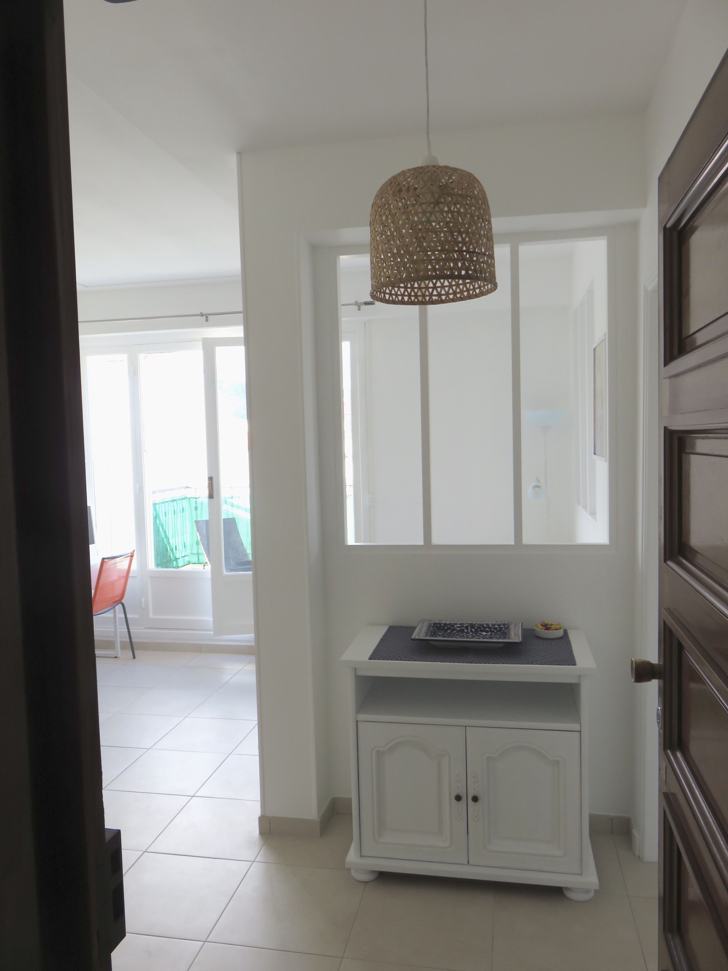 A hallway with a white cabinet, a hanging woven light fixture, and a door leading to a balcony.