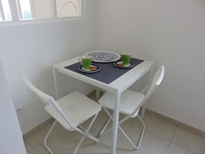 A small white table with two chairs, a green cup, a plate with a cookie, and a blue placemat.