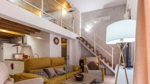 Un soggiorno moderno con divano, poltrone, tavolino e una scala che conduce a un piano superiore.