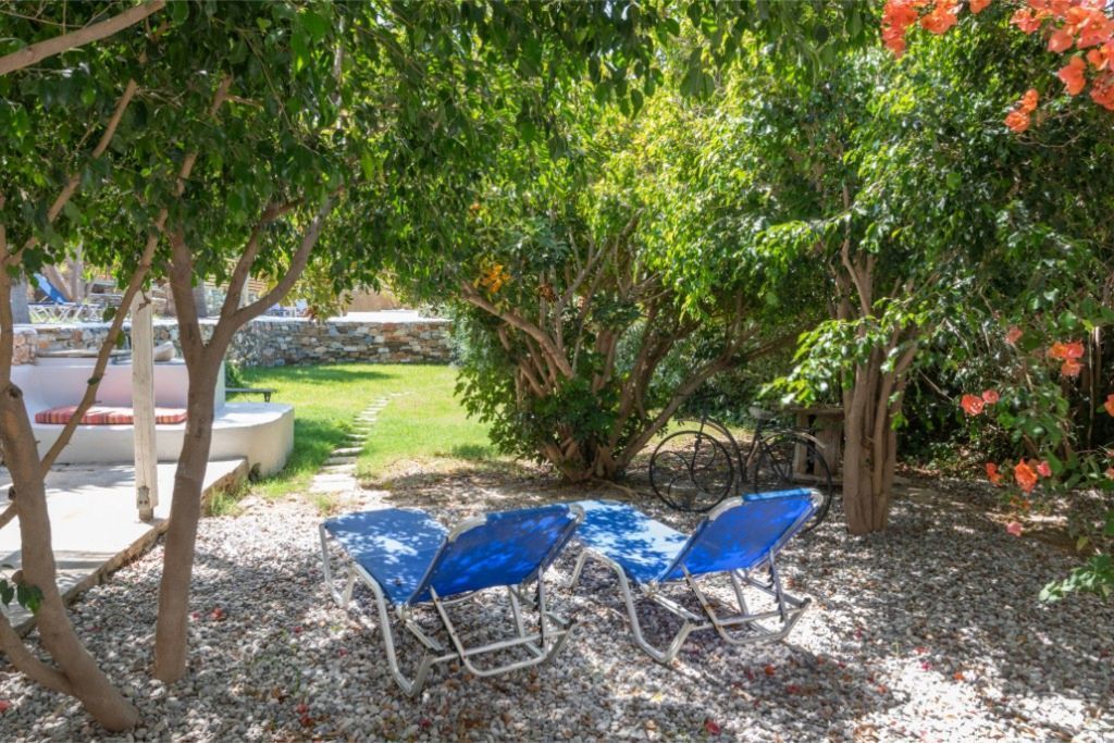 Eine Terrasse mit zwei blauen Stühlen und einem Tisch, umgeben von Bäumen und einem Garten.