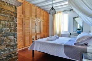 A bedroom with a stone wall, wooden wardrobe, bed with white bedding, and a hanging light fixture.