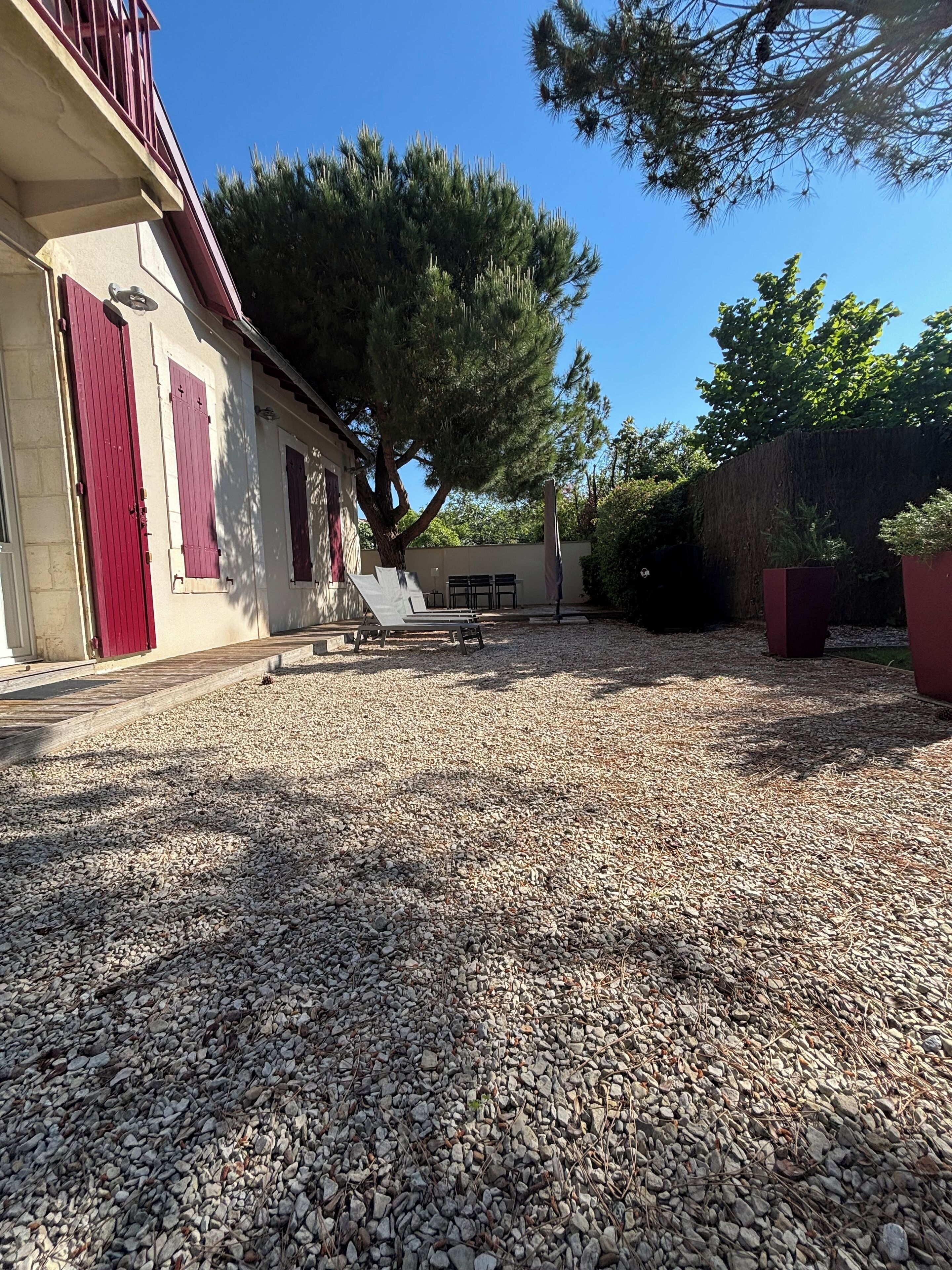 A building with red shutters, a gravel driveway, and a large tree in the background.
