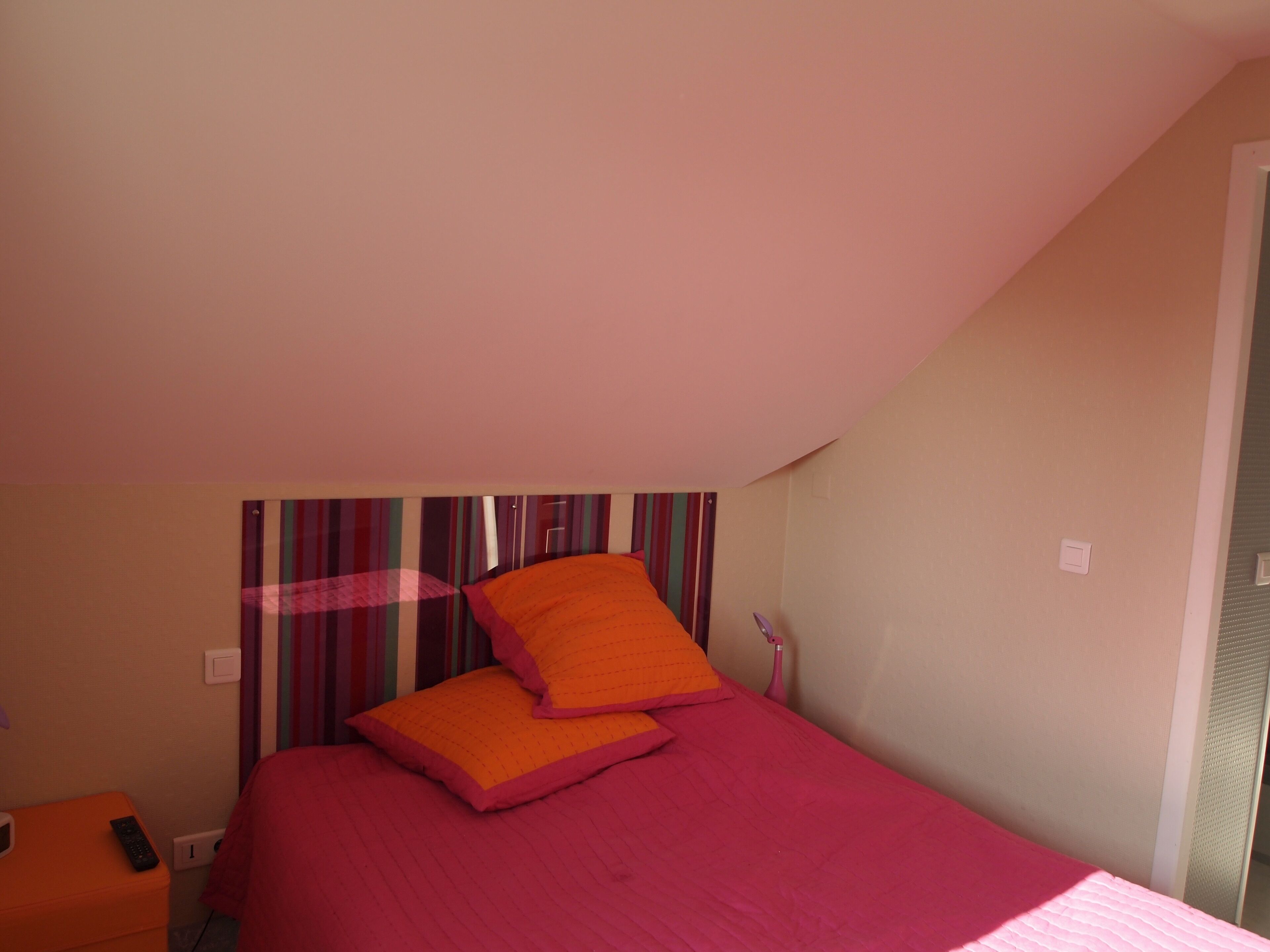 Quarto com cama, almofadas, mesa de cabeceira e cortina listrada.