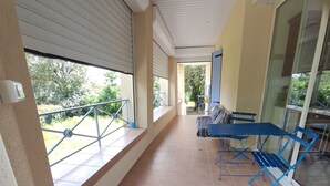 Um espaço coberto ao ar livre com piso de azulejos, cadeiras azuis dobráveis e uma porta de vidro que dá para o exterior.