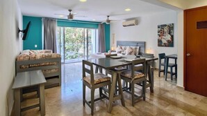 Una habitación con una cama, una mesa de comedor con sillas, un ventilador de techo y un ventanal con cortinas.
