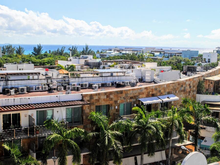 Terraço com várias unidades de ar condicionado, estrutura de edifício curvilínea e palmeiras.