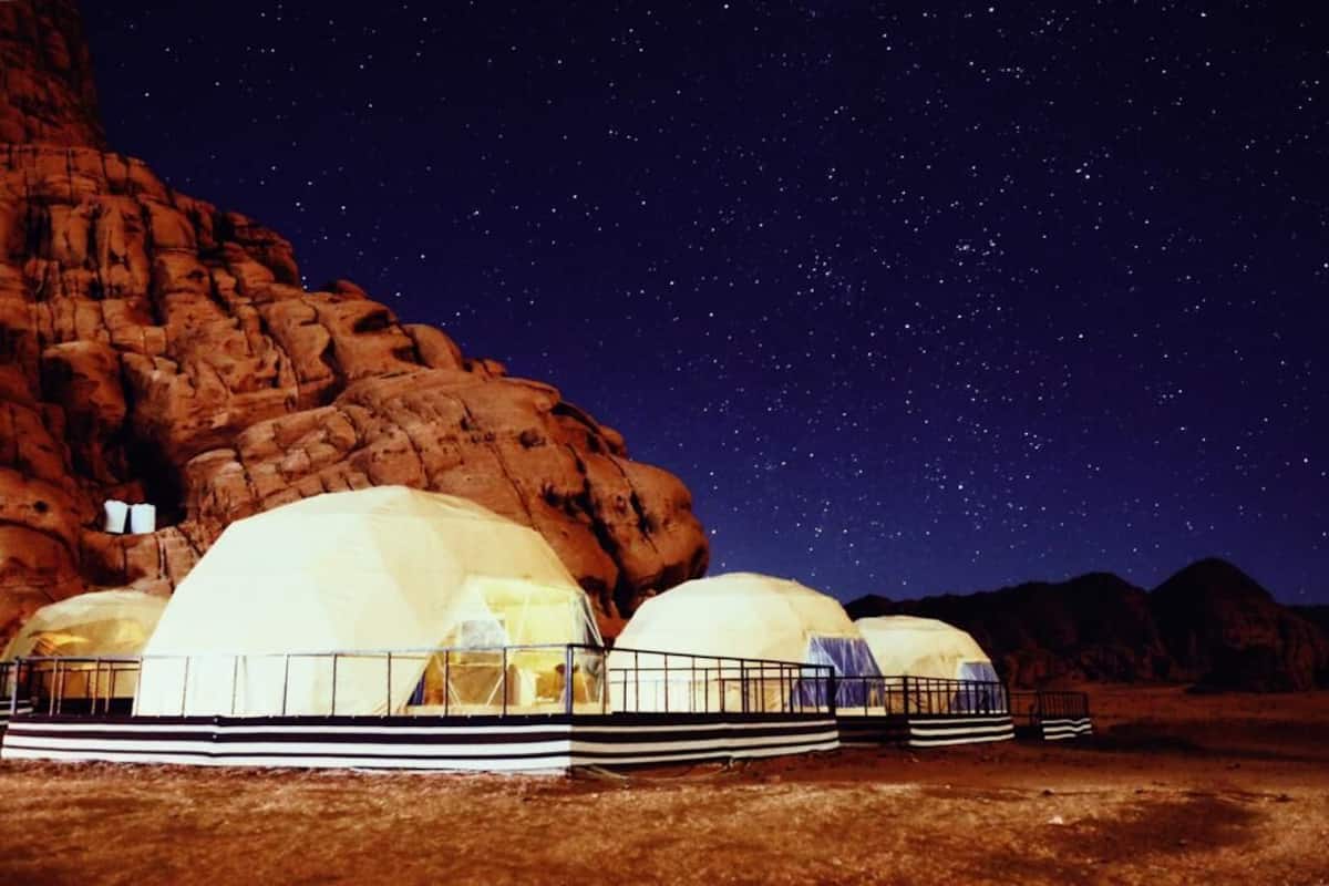 A series of dome-shaped tents with a metal railing in front, set against a rocky landscape under a starry night sky.