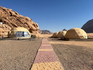 A desert landscape with multiple dome-shaped tents, a paved walkway, and rocky terrain. - Jamal rum camp (Wadi Rum)