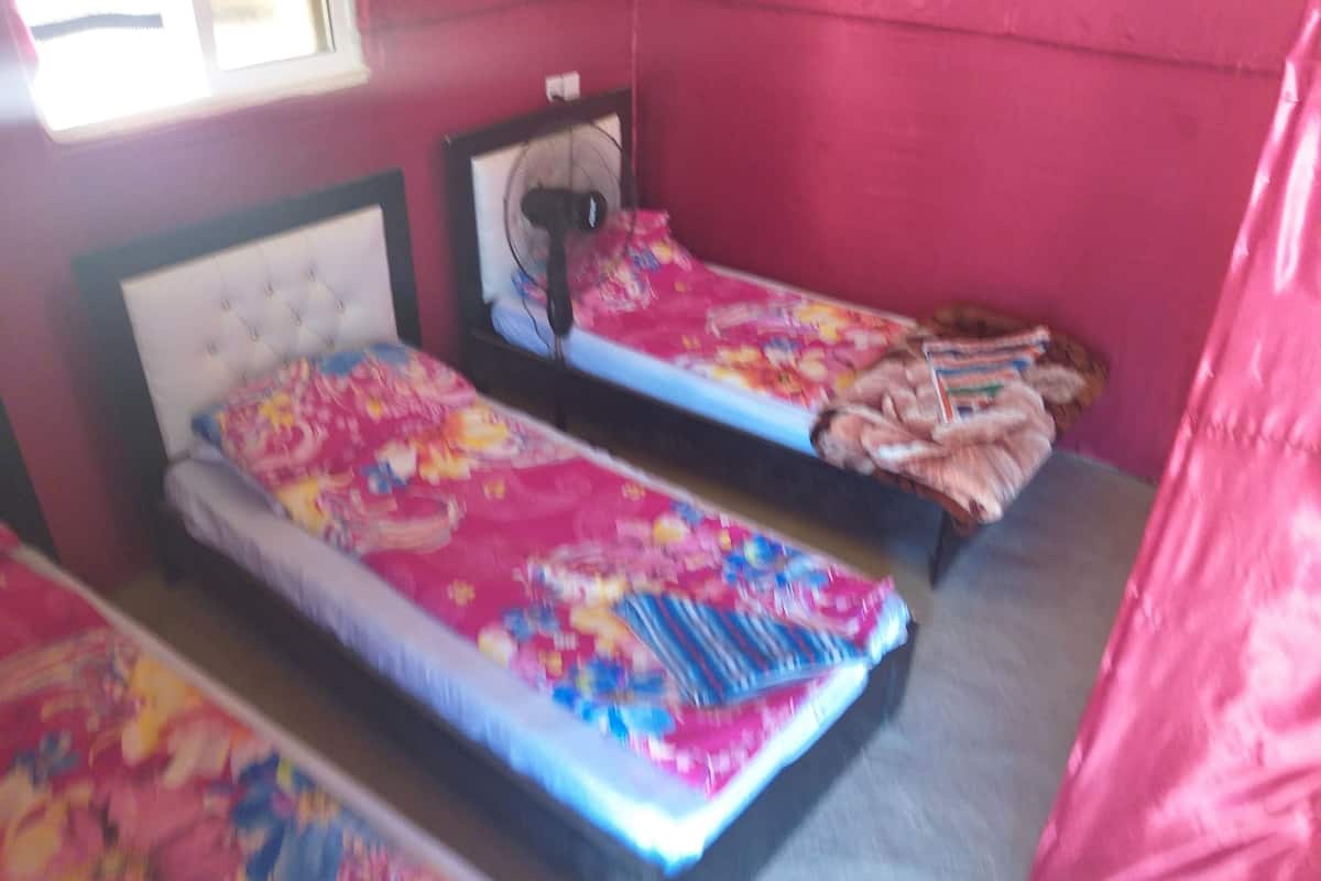 A room with two beds, each with a headboard and a bedside table. There is a window on the left side of the room.
