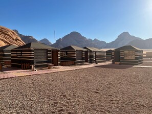 A row of striped tents with wooden doors and windows, set against a backdrop of rocky mountains and clear sky. - Jamal rum camp (Wadi Rum)