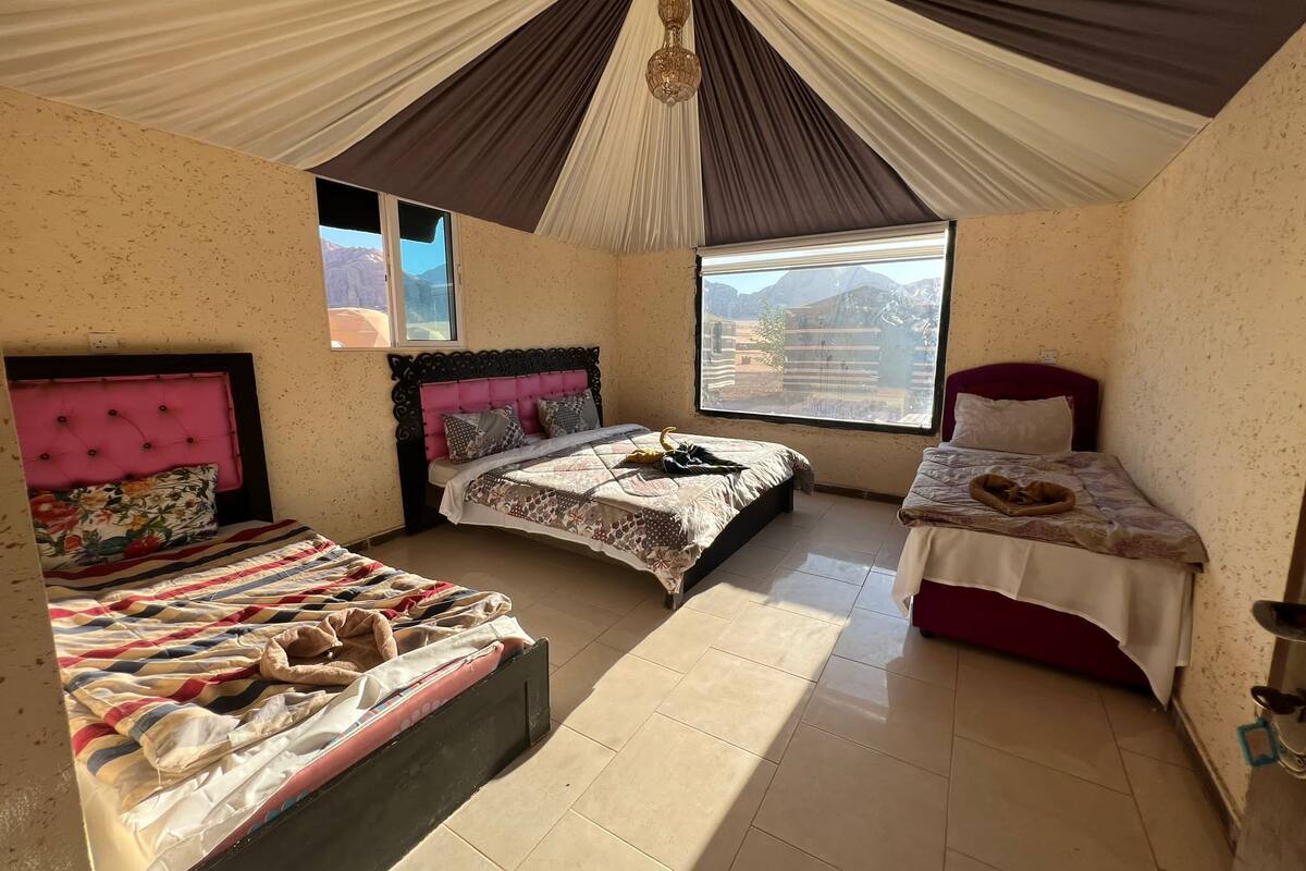 A room with three beds, a large window, and a view of mountains.