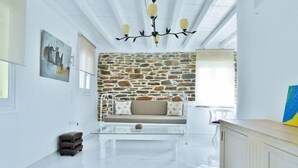 A modern living room with a stone wall, a glass coffee table, a sofa with patterned cushions, and a wooden cabinet. - Cozy 2-bedroom House in Tinos (Tinos)