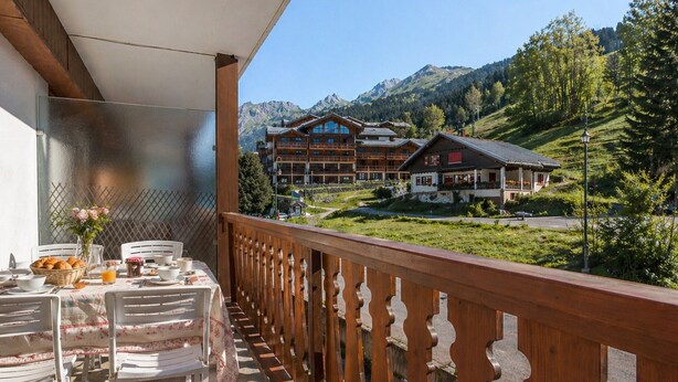 A balcony with a table set for breakfast, overlooking a mountain resort with buildings and trees. - 2** Apartment for 6, South, near slopes and shops (La Clusaz)