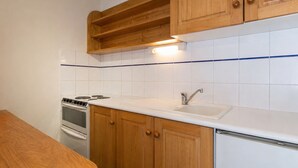 A kitchen with wooden cabinets, a white countertop, a stove, and a sink. - 2** Apartment for 6, South, near slopes and shops (La Clusaz)