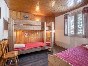 A room with two bunk beds, a wooden chair, a window with curtains, and a sign indicating room numbers.