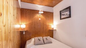 A wooden-paneled room with a bed, two wall-mounted lamps, and a framed picture on the wall. - 2** Apartment for 6, South, near slopes and shops (La Clusaz)